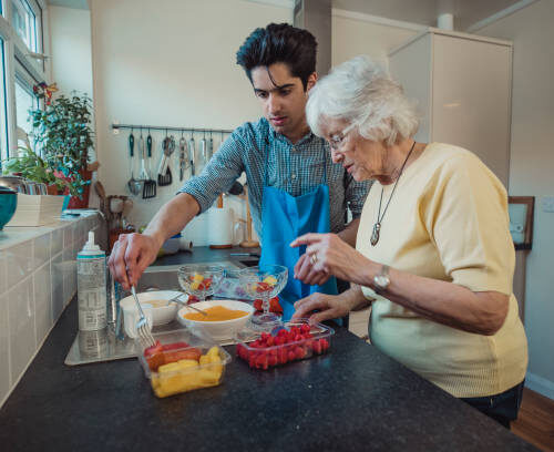 Teenage boy making fruit compote with his grandmother in the kitchen of her home.