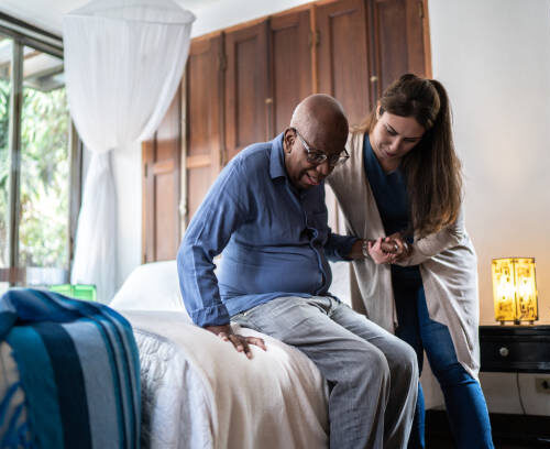 Home caregiver helping a senior man standing up at home