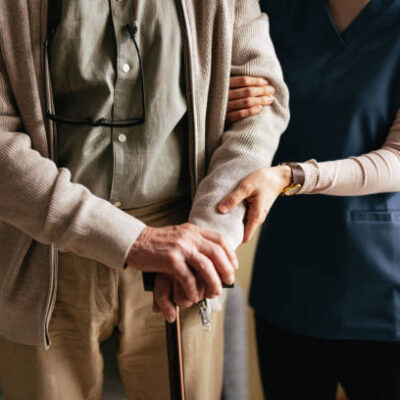 An anonymous Japanese female caregiver supporting elderly patient to stand and walk with a walking cane at the nursing home.